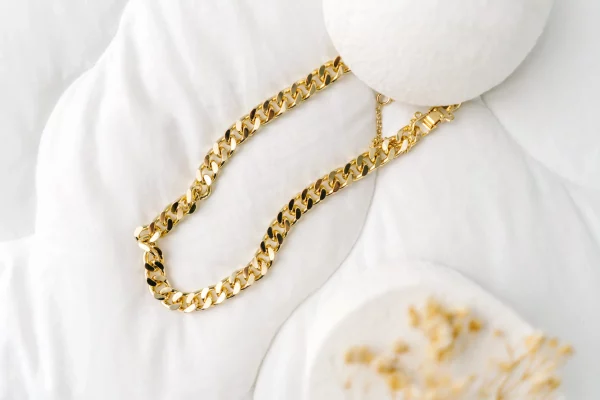 Imitation jewelry, Golden bijouterie chain on white textile background.