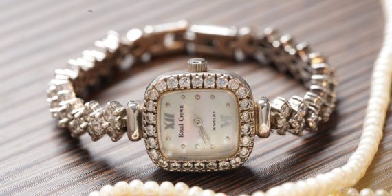 Womans Diamond Watch sitting on table next to pearl necklace